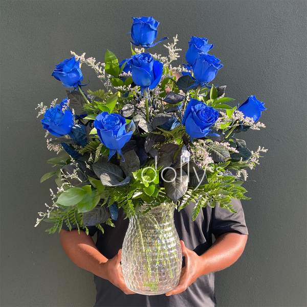 Blue roses arranged in a clear glass vase with mixed greenery