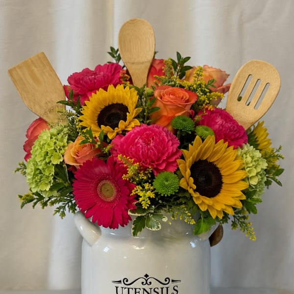 Bright mixed flower arrangement in a white utensil jar with wooden kitchen tools