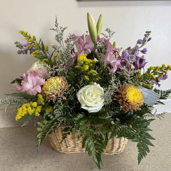 Mixed bouquet in a wicker basket with pink lilies, white roses, and yellow flowers