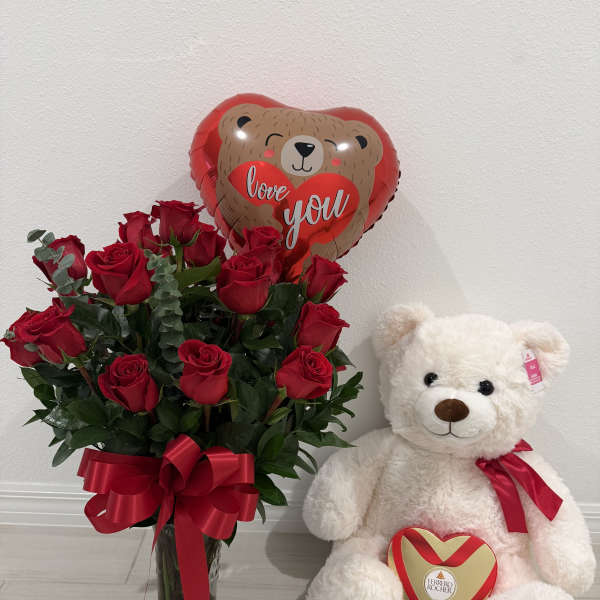 Red roses in a glass vase with a teddy bear, heart balloon, and chocolate box