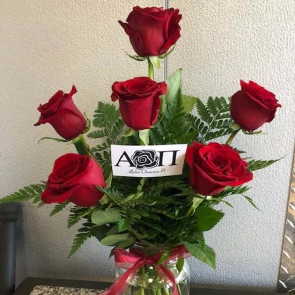 Six red roses arranged in a clear glass vase with a red ribbon