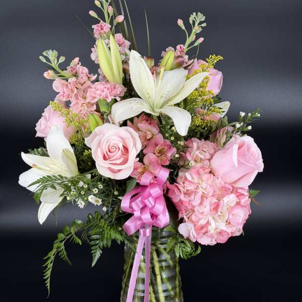 Pink roses and lilies arranged in a glass vase with a pink ribbon