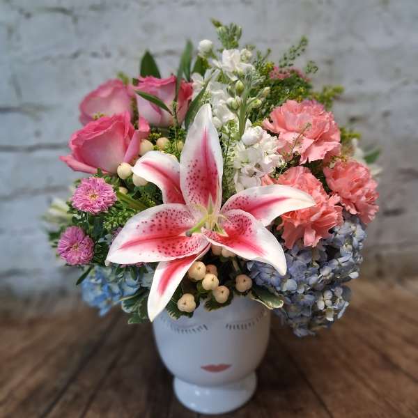 Mixed bouquet with pink roses, lilies, hydrangeas, and carnations in a white vase