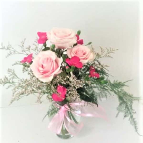 Pink roses and hot pink blooms in a clear vase with a pink ribbon