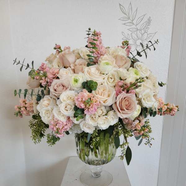 Large blush and white rose arrangement in a glass pedestal vase