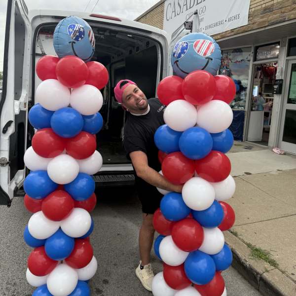 Red, white, and blue balloon columns with smiley-face balloons outside a shop