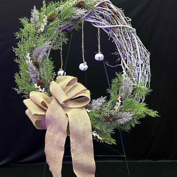 Rustic wreath with greenery, pinecones, and a burlap bow on a stand