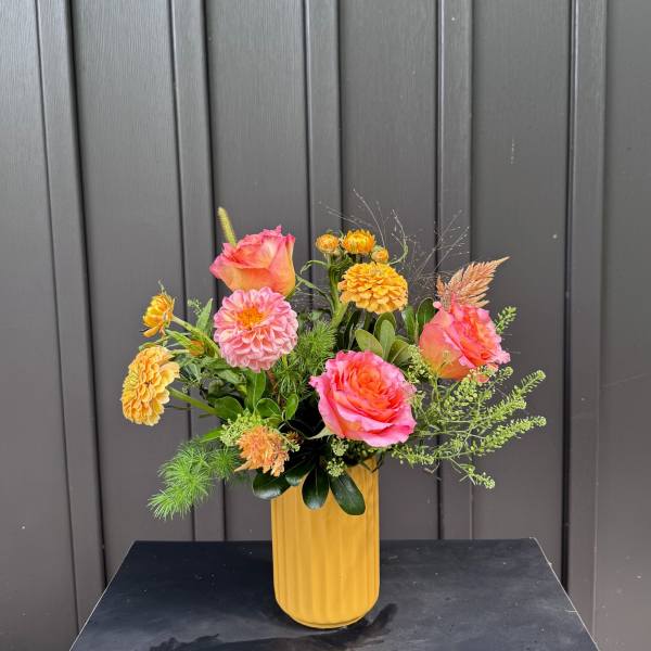 Pink and orange roses with yellow blooms in a tall yellow vase