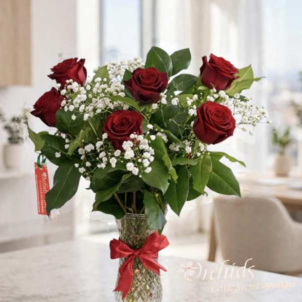 Red roses with white baby's breath in a clear glass vase tied with a red ribbon