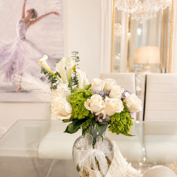 White roses and calla lilies in a glass vase with a ribbon bow