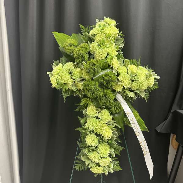 Green floral standing cross with a white ribbon on an easel