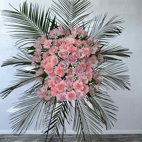 Pink floral standing spray with palm fronds on an easel