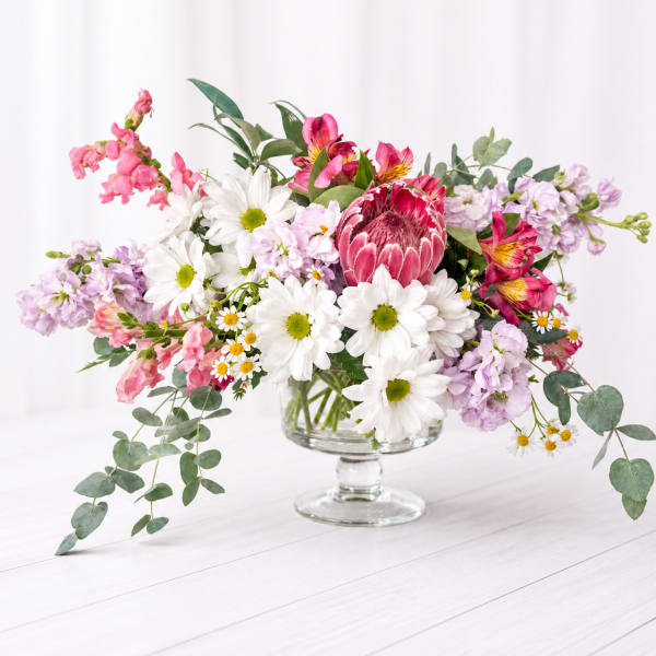 Mixed bouquet in a clear glass pedestal vase with pink, white, and lavender flowers