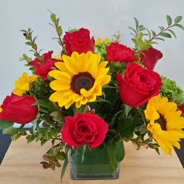Red roses and yellow sunflowers in a square glass vase