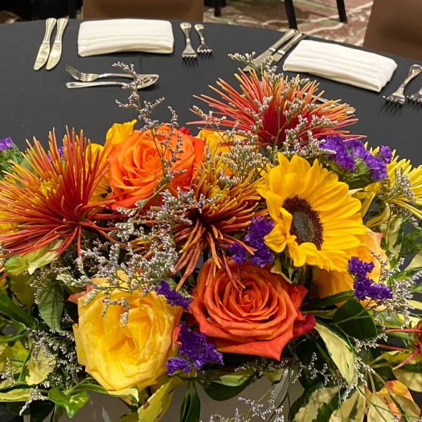 Bright mixed flower centerpiece with roses and sunflowers on a round table