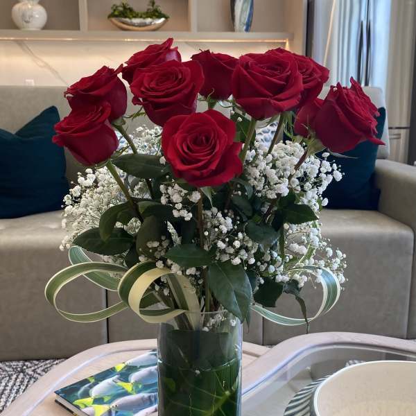 Red roses arranged in a tall glass vase with white baby's breath