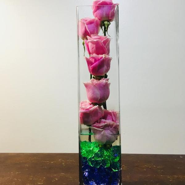 Pink roses in a tall clear glass vase with blue and green stones