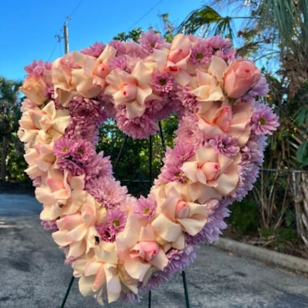 Heart-shaped floral wreath with pink and peach blooms on a stand