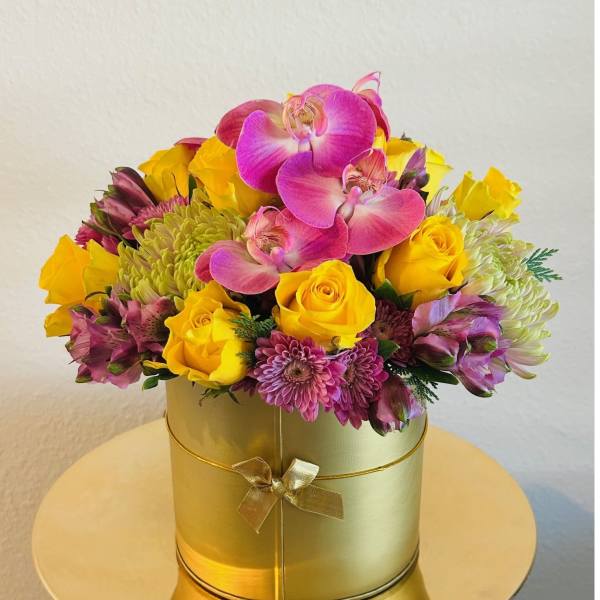 Pink orchids and yellow roses in a gold round box