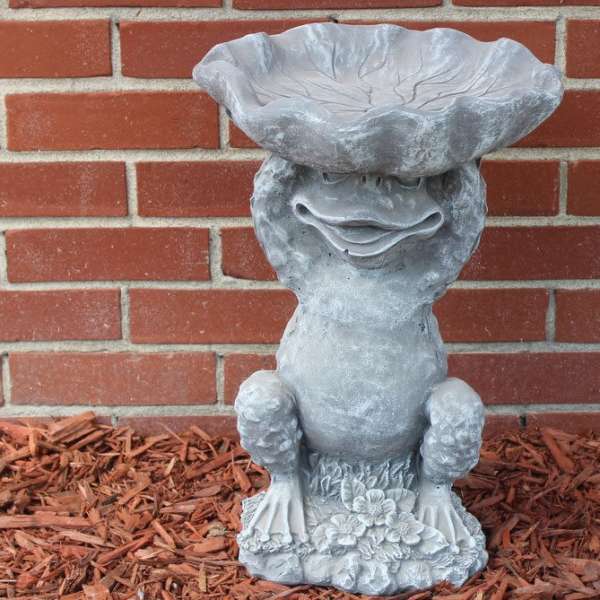 Gray garden frog statue against a brick wall