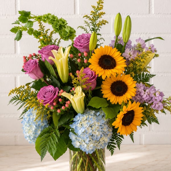 Mixed bouquet with sunflowers, roses, lilies, and hydrangeas in a glass vase