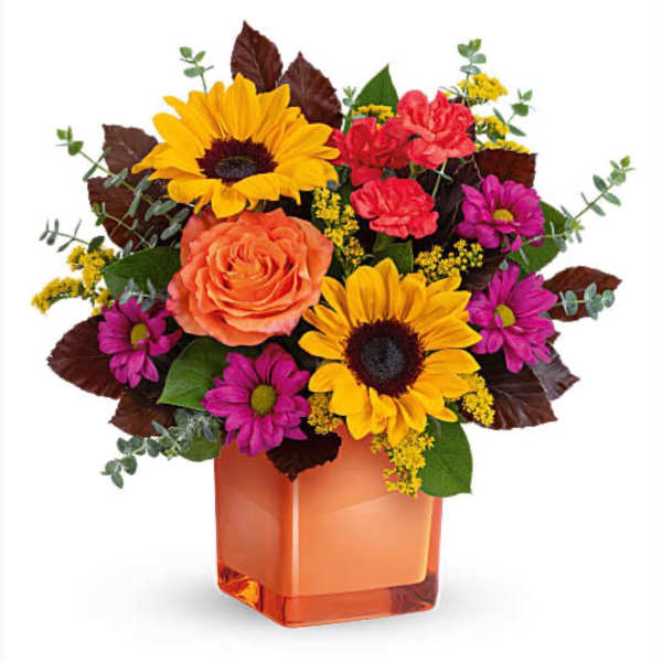 Mixed bouquet with sunflowers, roses, and daisies in an orange glass vase