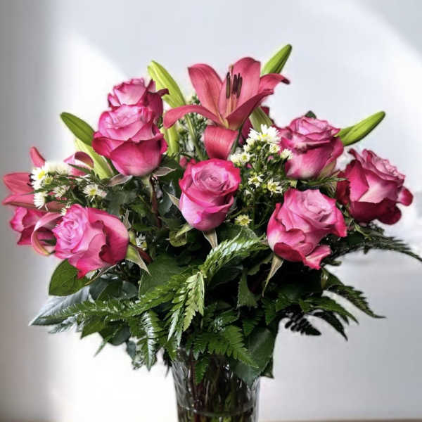 Pink roses and a lily arranged in a clear glass vase
