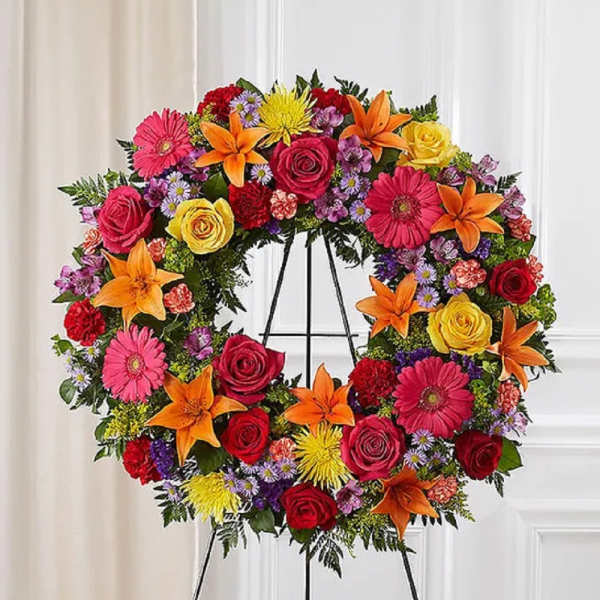 Large circular funeral wreath with roses, lilies, and daisies on an easel