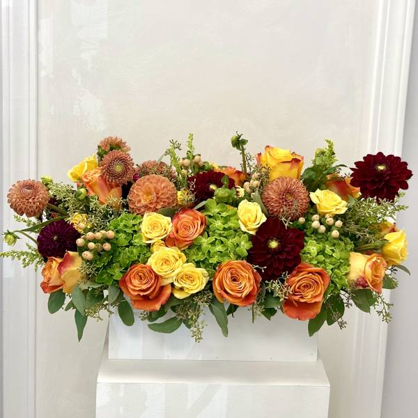Mixed bouquet of orange, yellow, and burgundy flowers in a white container