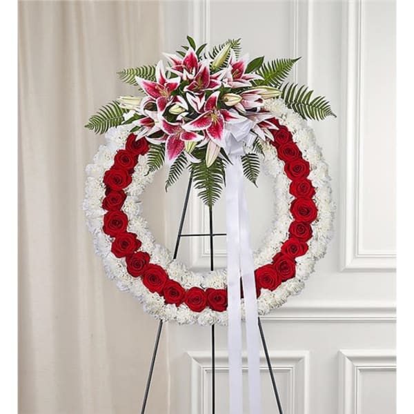 Circular funeral wreath of red roses and white flowers with lilies on a stand