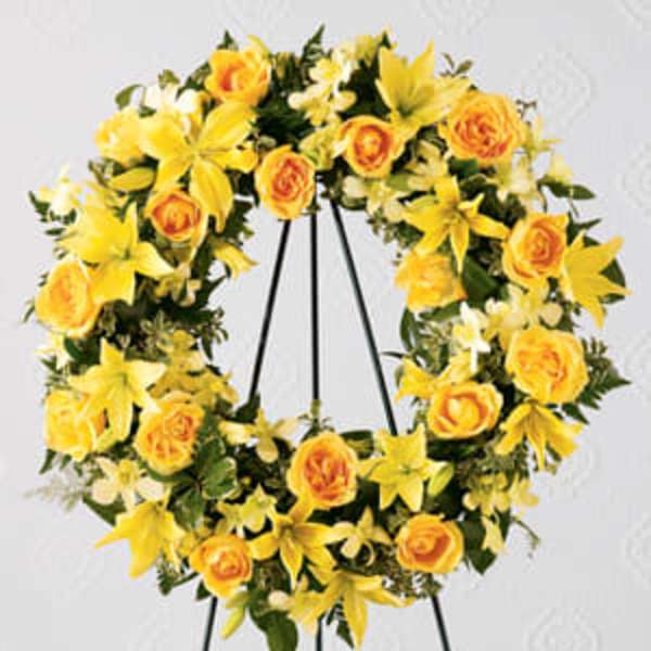 Yellow floral wreath with roses and lilies on a black stand