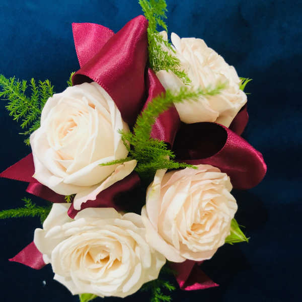 Cream roses with burgundy ribbon and green filler on a dark background