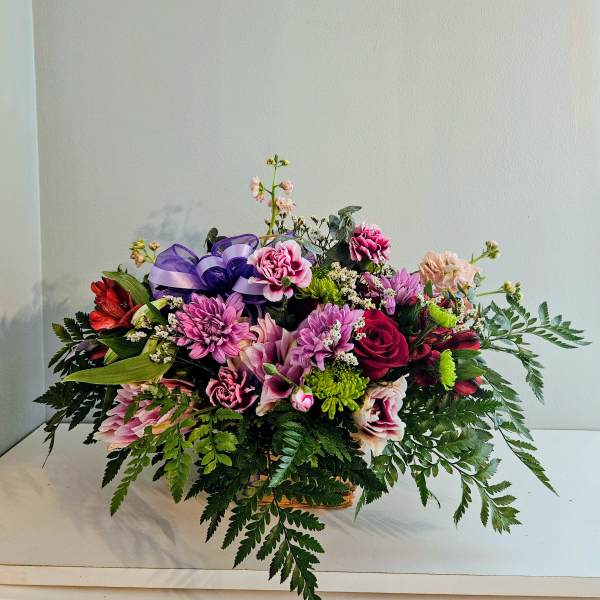 Mixed bouquet of pink and purple flowers in a basket with a purple ribbon