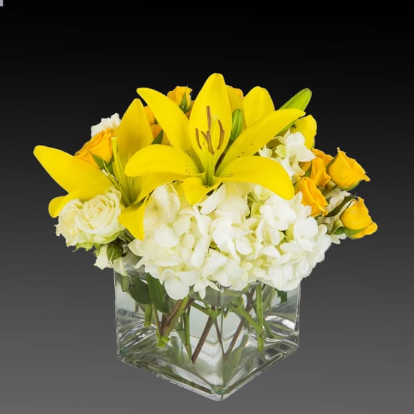 Yellow lilies and white flowers in a clear square vase