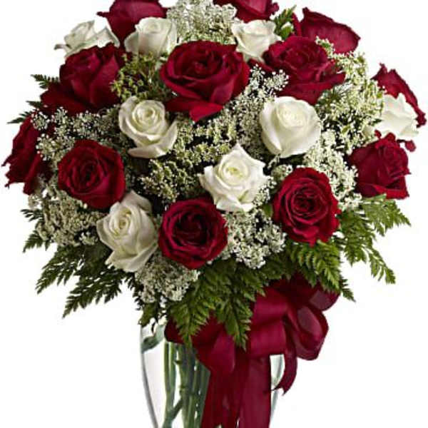 Red and white roses arranged in a clear glass vase with a red ribbon