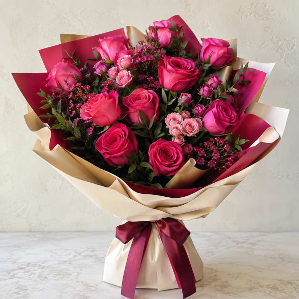 Bouquet of hot pink roses and spray roses wrapped in cream and burgundy paper