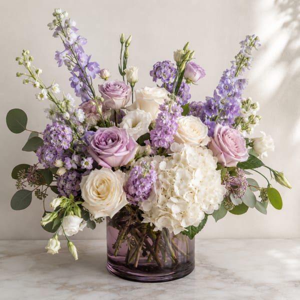 Lavender and white floral arrangement in a purple glass vase