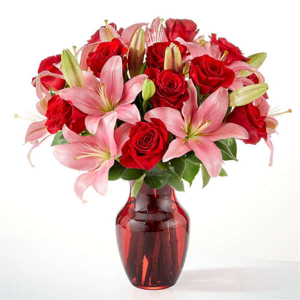 Bouquet of red roses and pink lilies in a red glass vase