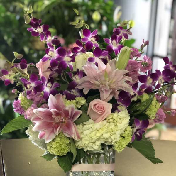 Pink lilies, roses, hydrangeas, and purple orchids in a clear glass vase