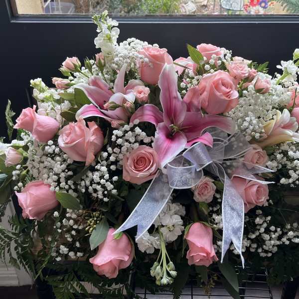 Large pink rose and lily arrangement with white filler flowers and a silver ribbon