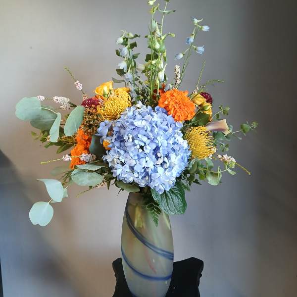 Mixed bouquet in a tall glass vase with blue hydrangea and orange flowers