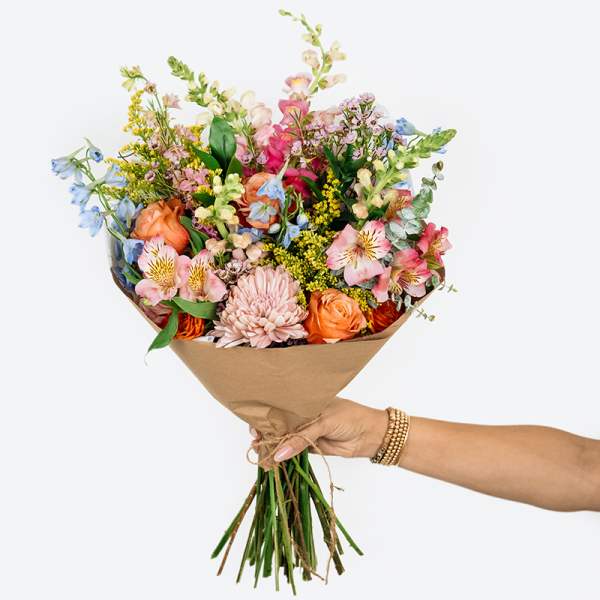 Handheld bouquet of mixed pastel flowers wrapped in brown paper