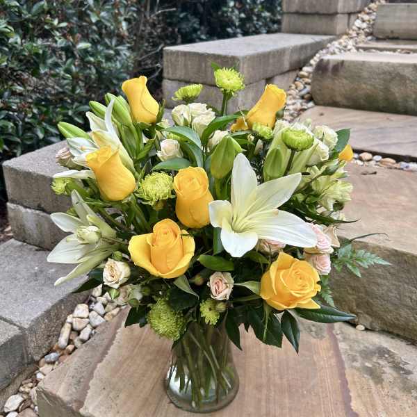 Yellow roses and white lilies arranged in a clear glass vase
