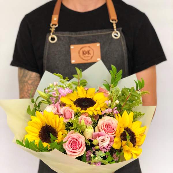 Hand-tied bouquet of yellow sunflowers and pink roses wrapped in pale paper
