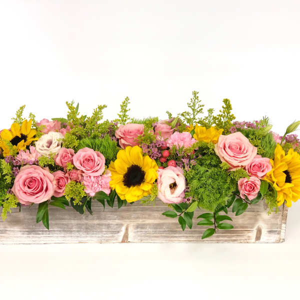 Low centerpiece of pink roses, yellow sunflowers, and green accents in a rustic whitewashed wooden box