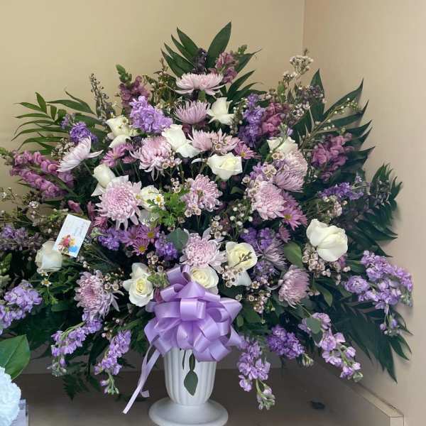 Large lavender and white floral arrangement in a white urn with a purple bow