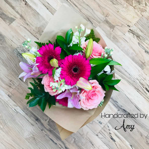 Bouquet of pink gerbera daisies, roses, and lilies wrapped in brown paper