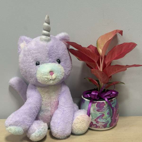 Plush unicorn beside a potted red-leaf plant in a decorative can
