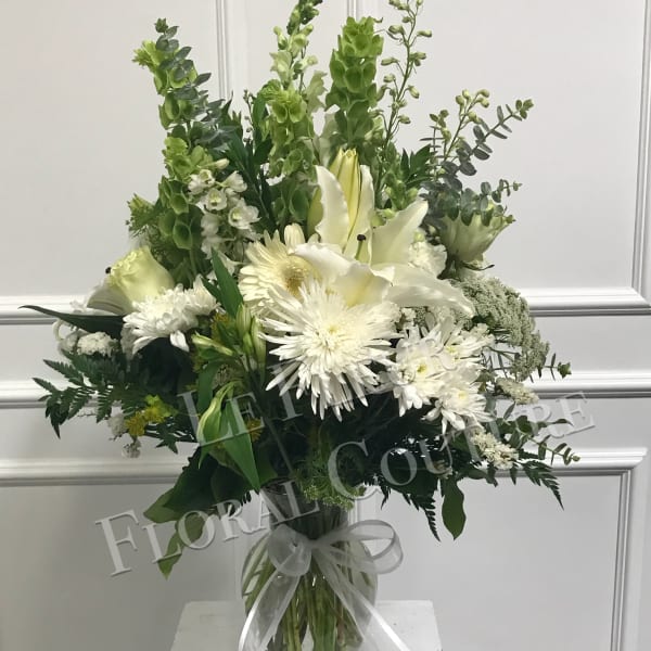 White and green floral arrangement in a glass vase with a ribbon