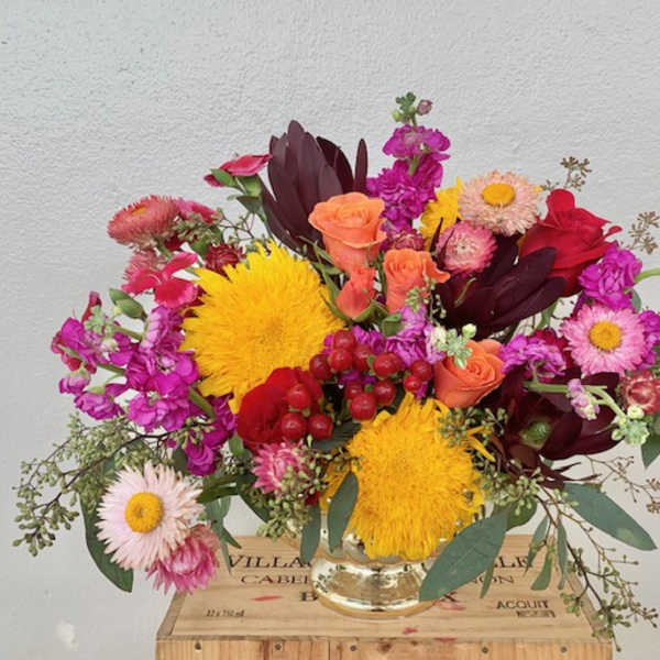 Colorful mixed bouquet in a clear glass vase with yellow, pink, red, and peach blooms.